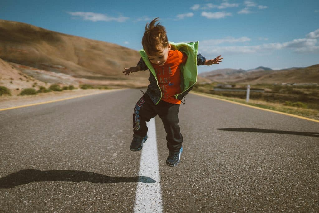 A young boy jumps happily in the air in the middle of a desert road in the United States.