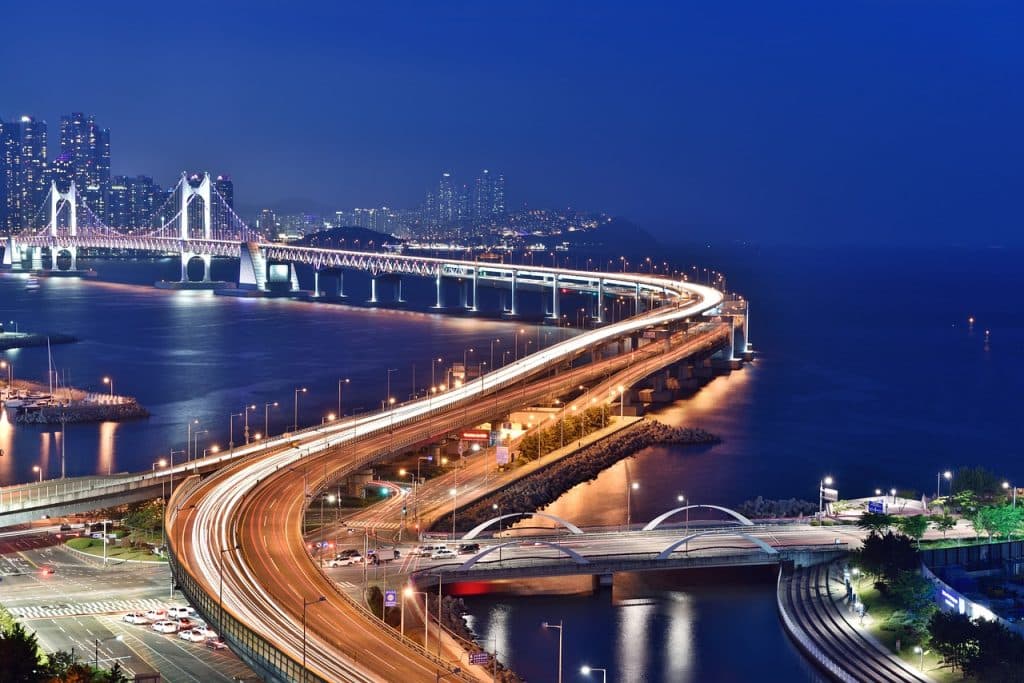 City of Busan in South Korea, photographed at night. The bridge spanning the sea is lit up along its entire length, the streets are empty.