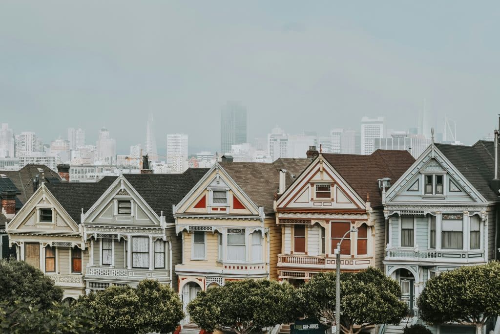 Charming little terraced houses in San Francisco in the United States. They are lined with trees. Skyscrapers can be seen in the background of the photo.