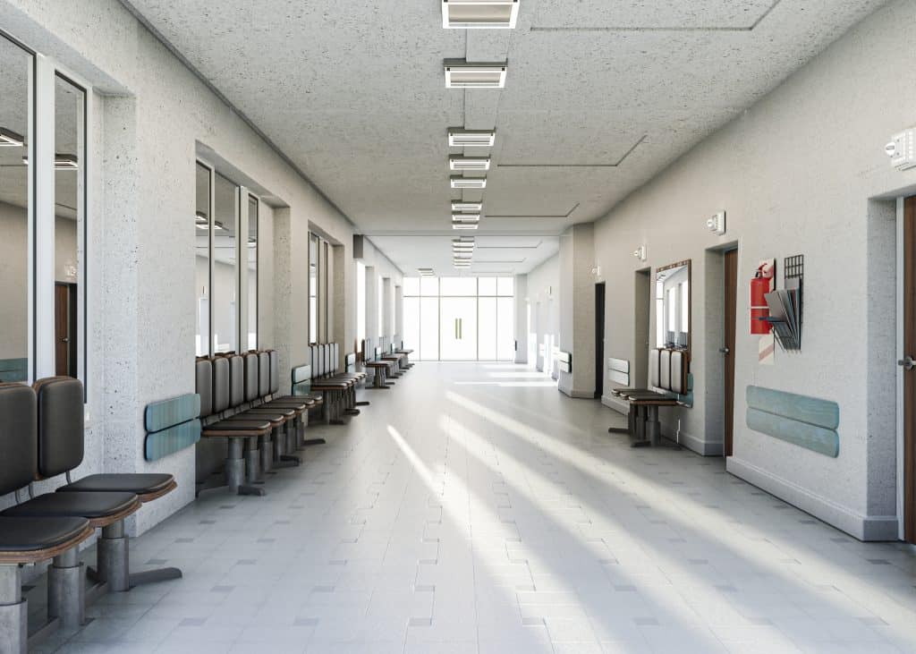 Empty hospital corridor leading to operating theatres and patient waiting rooms, with chairs on both sides.