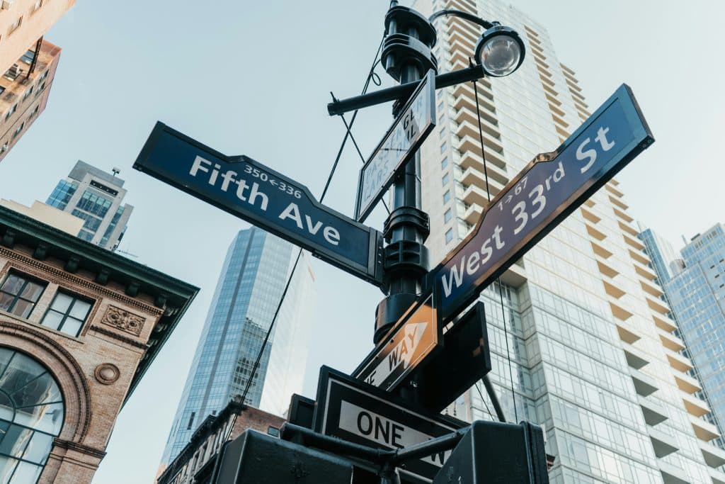 Low-angle photo of black signs pointing the way up Fifth Avenue and West 33rd Street in New York, hanging from a lamppost.