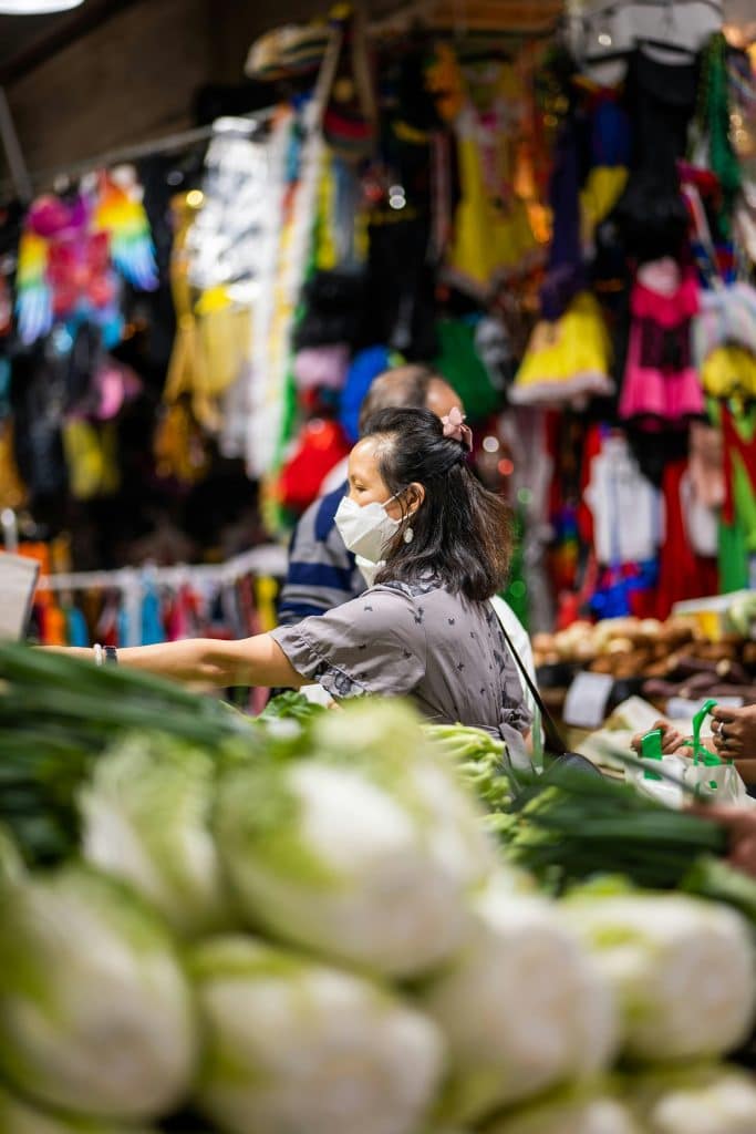 A Korean woman sells her products at a stall in a covered market in South Korea. She wears a mask and tidies up her stall.