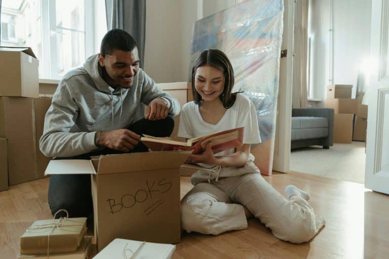 A young couple who have just moved into their new house are reminiscing as they read a book they have taken out of the boxes. They are sitting on the living room floor.