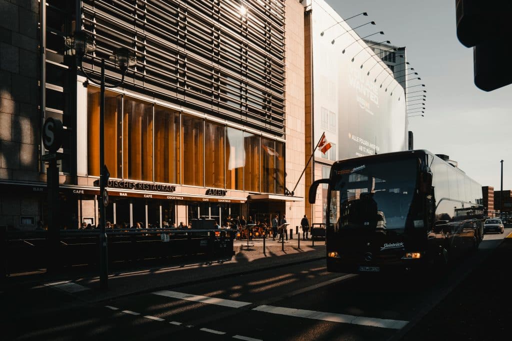Photo of a street in Berlin, a bus has stopped at a red light. The photo was taken at the end of the day, with the sun reflecting on the windows of a building.