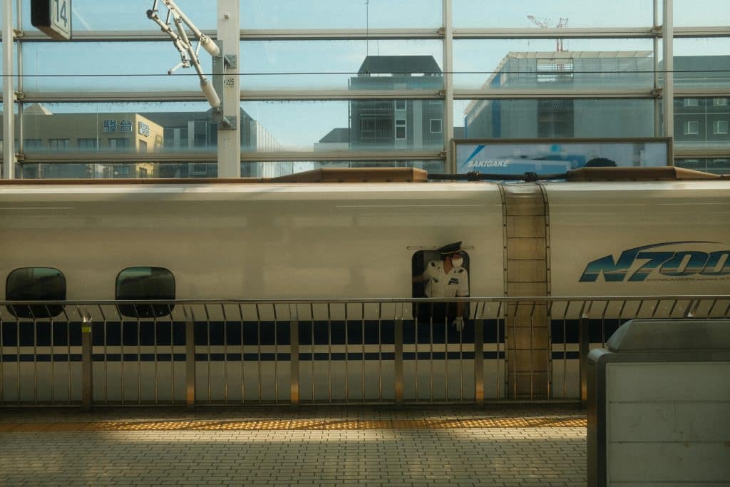 Photo of a Japanese officer sticking his head out of the window of a train stopped at the platform. The train station has glass windows, the photo was taken on a beautiful day.