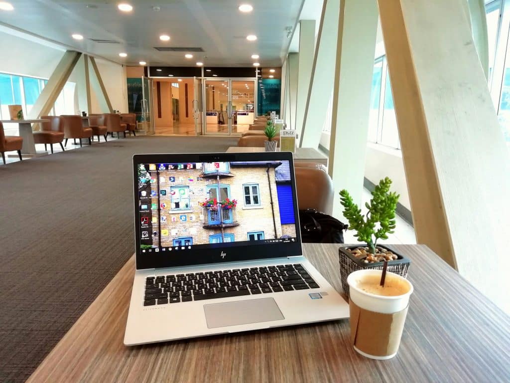 Black and silver laptop belonging to a digital nomad resting on a table in a luxurious coworking space. A cup of coffee is sitting next to the laptop.