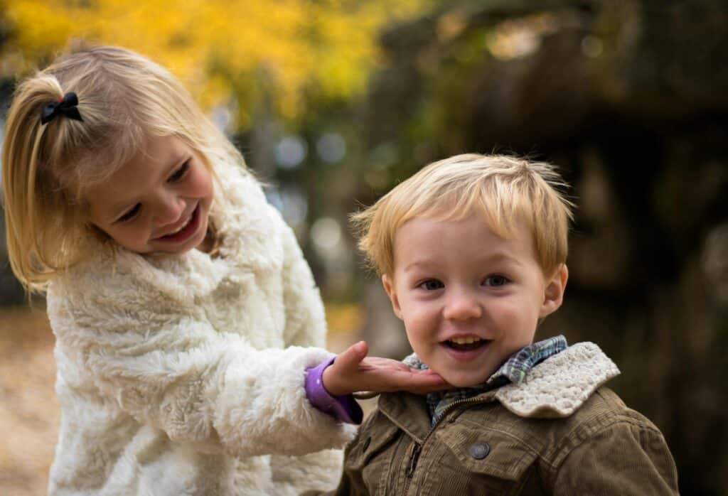 A little girl laughs with her little brother and holds him gently by the chin. They are dressed warmly for the autumn season.