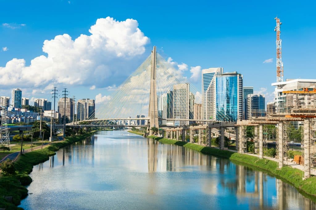 Grey concrete bridge over a river in Sao Paulo, Brazil. Skyscrapers can be seen on either side of the river.