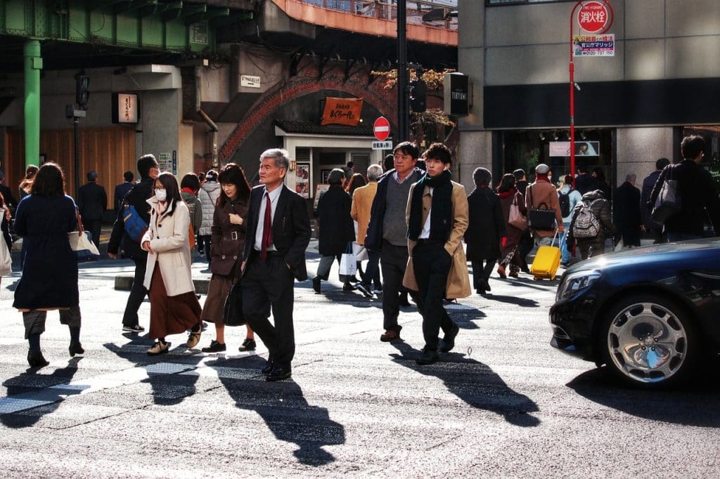 A moment from everyday life captured at a pedestrian crossing in Japan, where many residents cross the street. A car has stopped and is waiting its turn to pass. The photo appears to have been taken in autumn or winter, judging by the clothes the pedestrians are wearing.