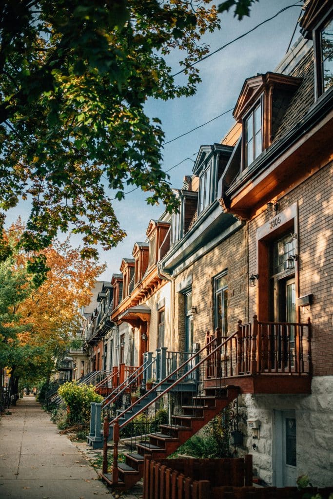 A pretty street in Montreal with terraced houses and trees lining the street. The houses are made of brown brick and are all similar and characteristic of houses on the American continent.