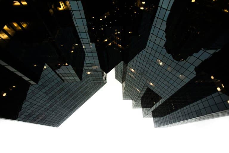 A monochrome, low-angle shot of large, modern, glazed buildings. The photo is uncluttered and conveys an atmosphere of modern urban life.